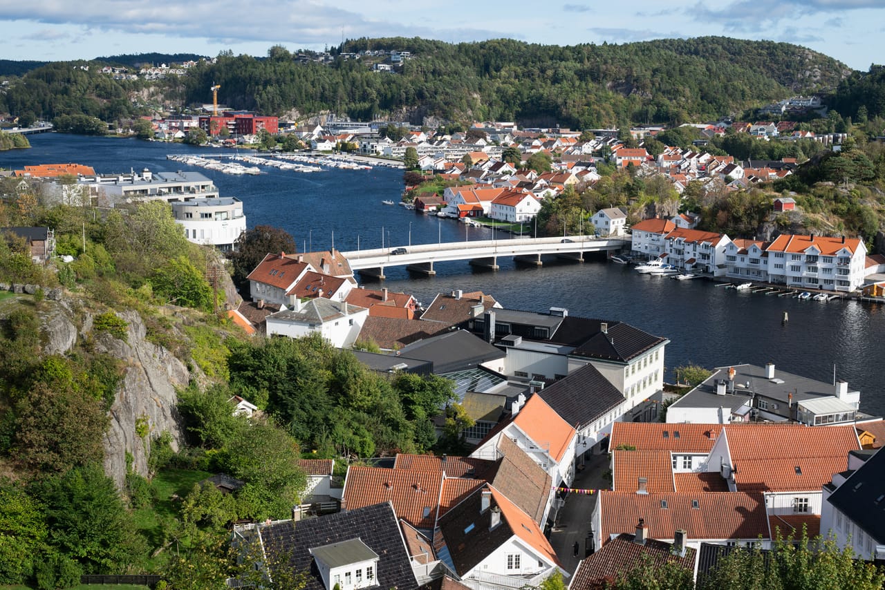 Utsikt fra Uranienborg over elva og brua i Mandal, med hvitmalte trehus langs bredden.