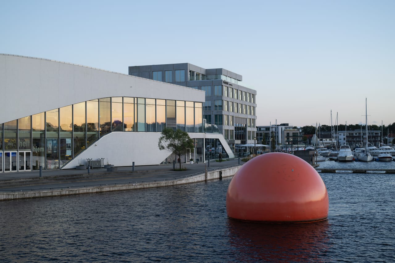 Buen kulturhus og en rød flytekule i havnebassenget i Mandal, fotografert i blåtimen.