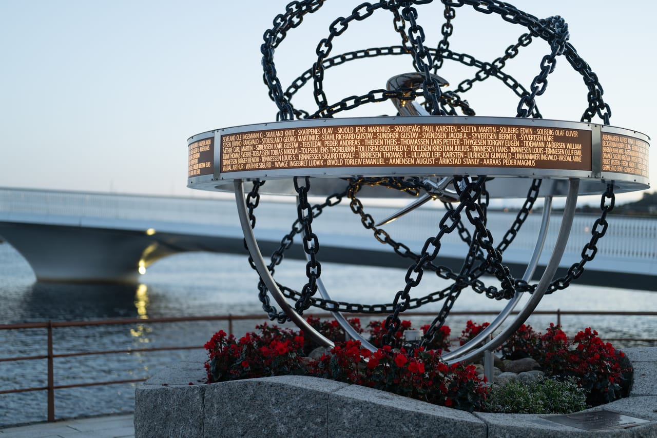 Minnesmerke med lenker og navn på falne fra andre verdenskrig, ved brua i Mandal i blåtimen.