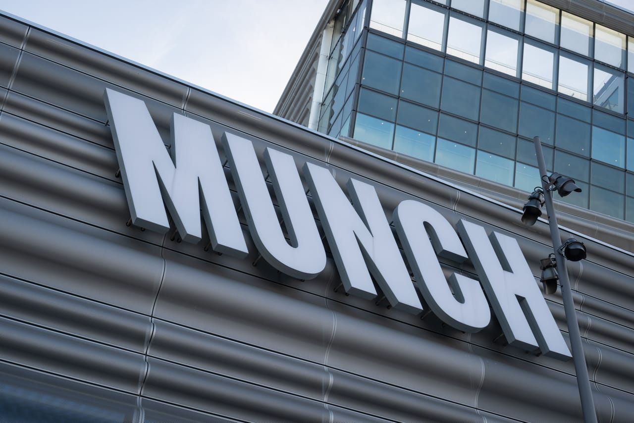 «MUNCH»-skiltet på den bølgete metallfasaden til Munch-museet, sett nedenfra mot blå himmel.