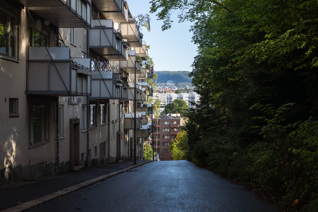 En bratt gate mellom boligblokker med balkonger, med utsikt ned mot byen og åsene i bakgrunnen.