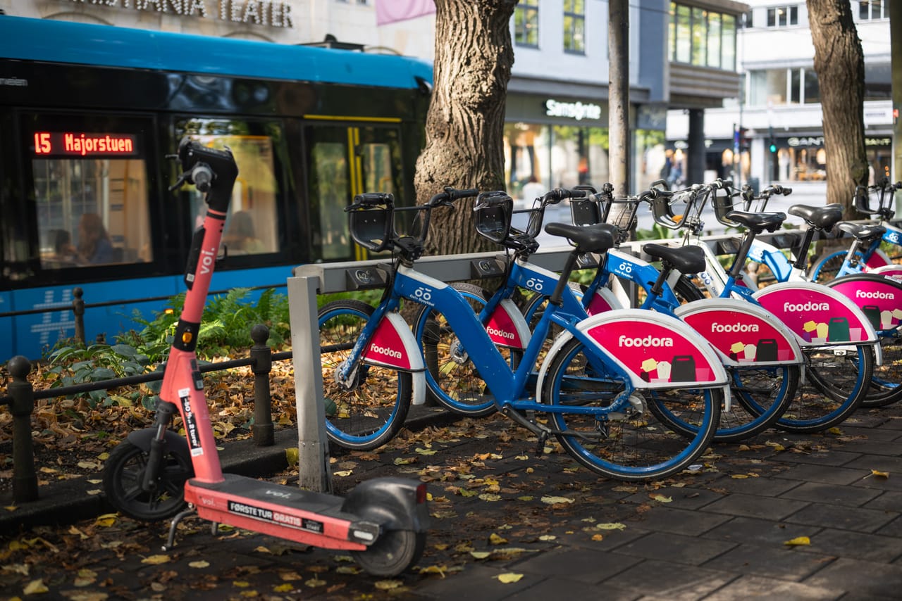 En trikk passerer Christiania Teater, med utleiesykler og en elsparkesykkel parkert i forgrunnen.