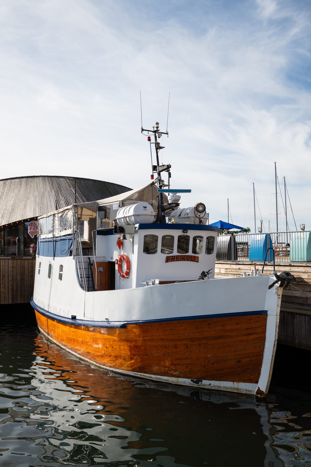 Den gamle trebåten «Freikoll» fortøyd ved brygga, med seilbåtmaster i bakgrunnen.