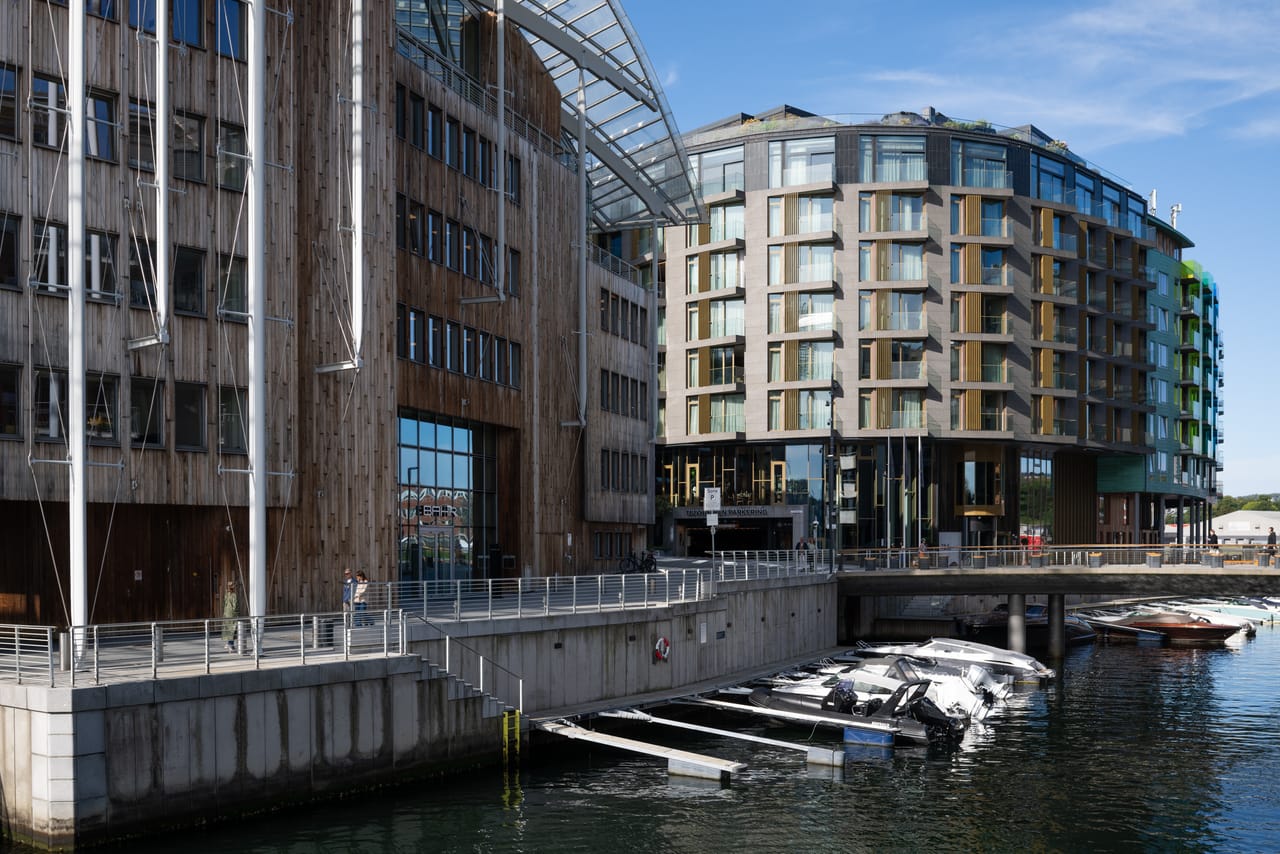 Bygningene på Tjuvholmen sett fra kanalen, med trekledning, glassfasader og båter fortøyd i småbåthavnen.