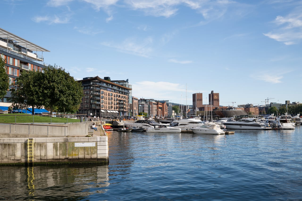 Utsikt langs havnepromenaden mot Oslo rådhus, med lystbåter fortøyd i forgrunnen.