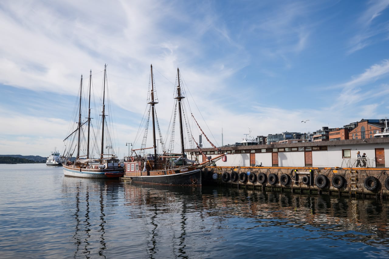 To gamle seilskuter fortøyd ved kai, med bildekk som fendere langs bryggekanten.