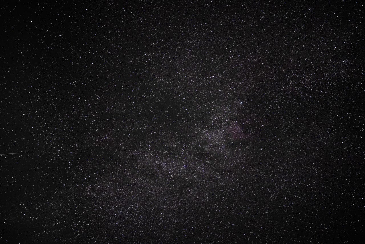 Stjernehimmel med Melkeveien som et lyst bånd med mørke støvskyer, og en tynn lysstripe nede til venstre.