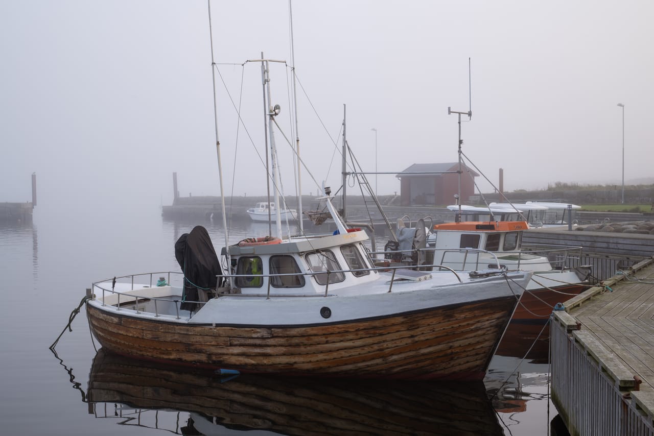 Gamle fiskebåter i tre ved brygga i Borhaug havn på Lista, innhyllet i tett tåke.